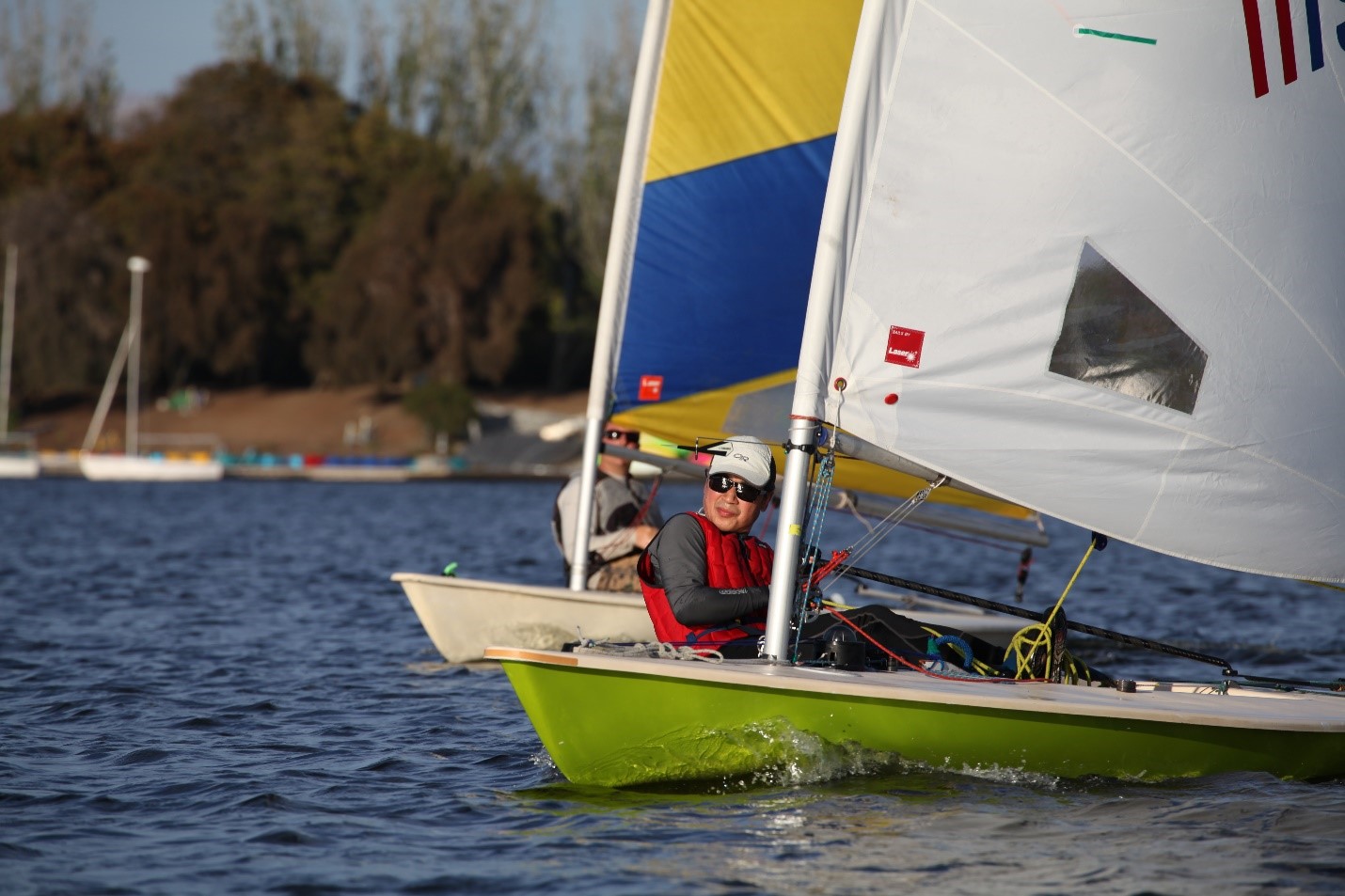 A man in a fast moving sail boat maneuvering it.