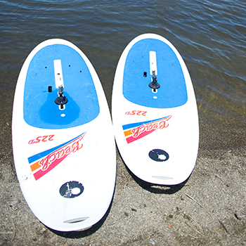 Two windsurfing boards sitting at the edge of the lake.